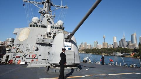 Auf dem Deck vor einer Haubitze steht eine dunkelhäutige Matrosin. 