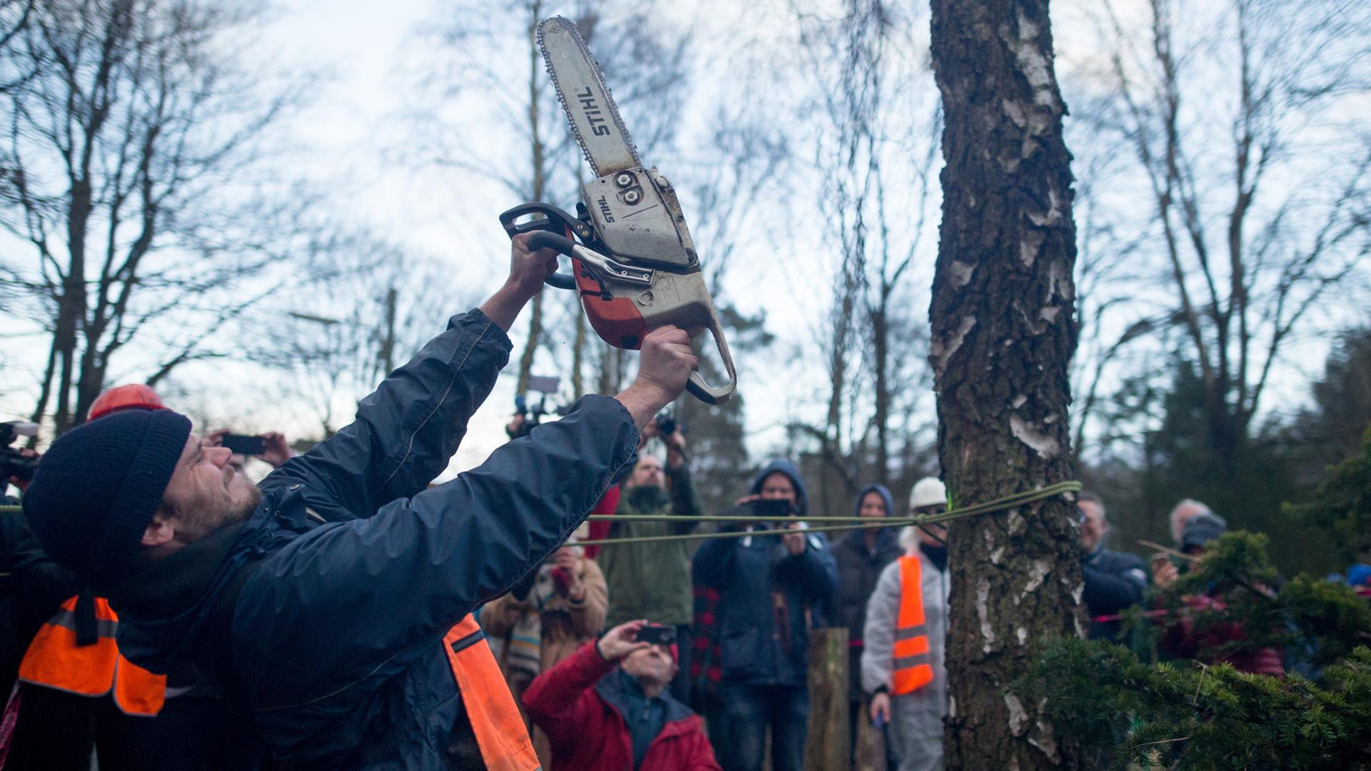Ein Demonstrant hält am in Hamburg vor einem Baum eine Kettensäge mit die Luft.