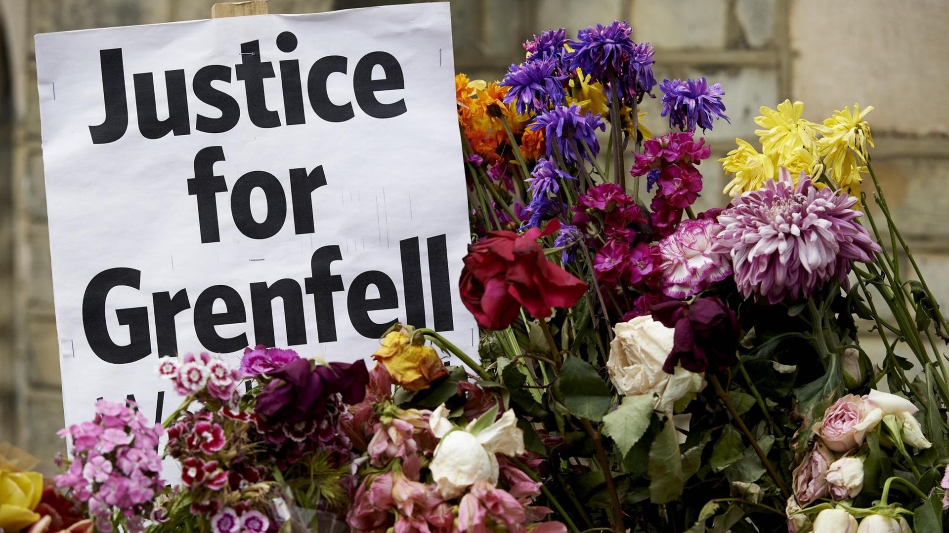 In Erinnerung an die Brandkatastrophe im Grenfell Tower in Londen stehen Blumen neben einem Zettel mit der Aufschrift "Justice for Grenfell"