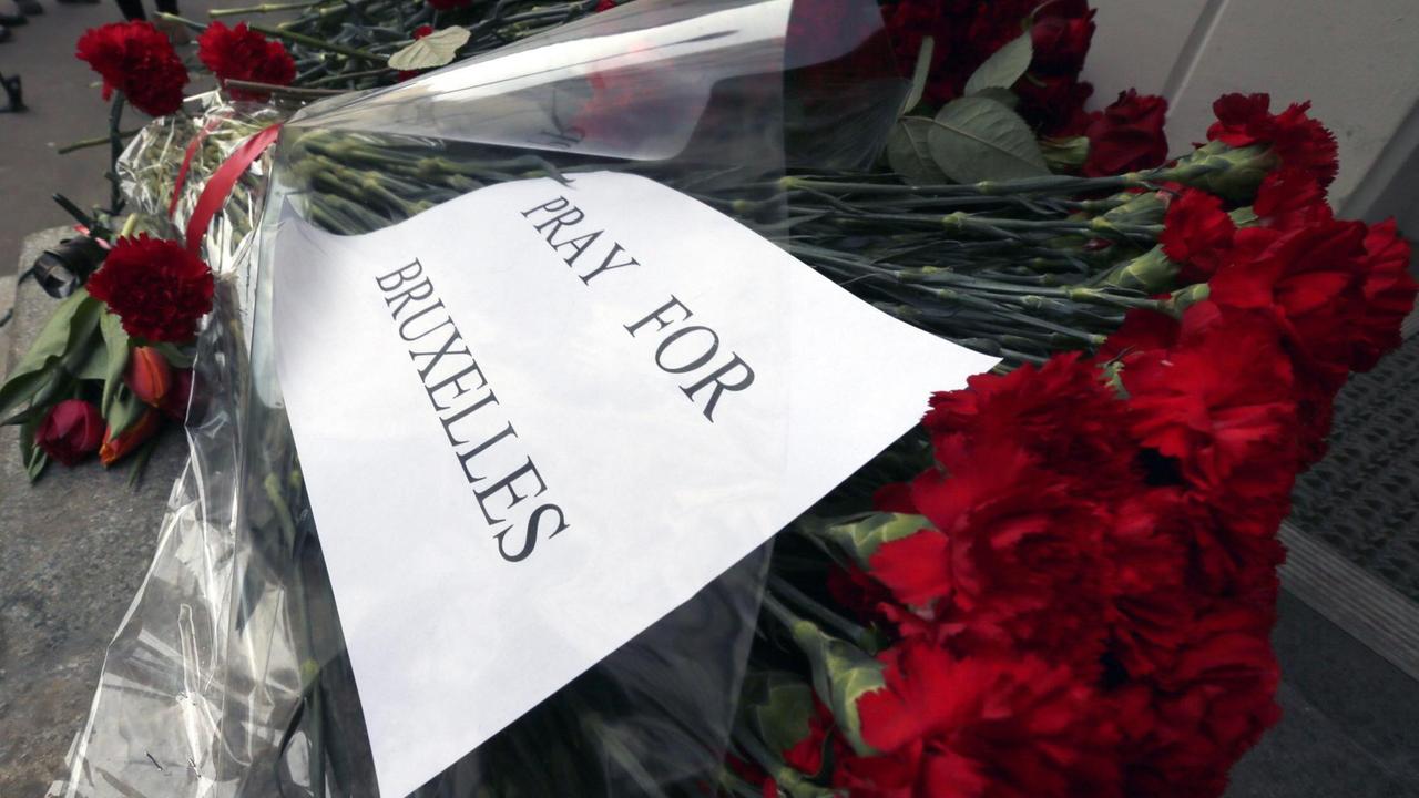Ein Schild mit der Aufschrift "Pray for Brussel" liegt auf einem Strauß Rosen.