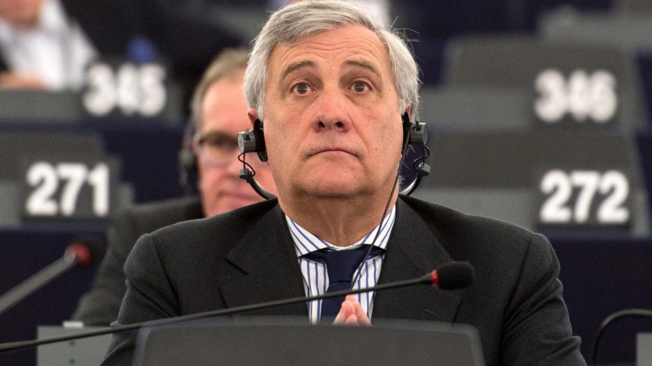 Tajani sitzt auf einem der Abgeordnetenplätze; er hat die Nummer 105. Dahinter weitere Abgeordnete auf nummerierten Plätzen.