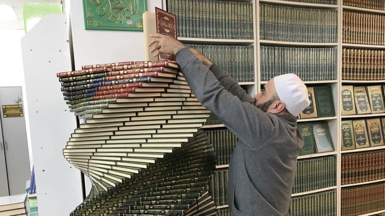 Ein Buchhändler stapelt in einer islamischen Buchhandlung in Machatschkala kunstvoll Bücher aufeinander, so dass sich eine Bücherspirale ergibt (Bild: Gesine Dornblüth)