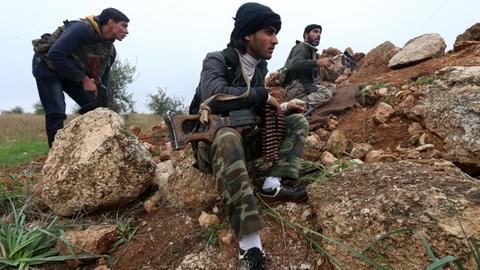 Drei bewaffnete Al-Nusra-Kämpfer kauern an einem steinigen Hügel.