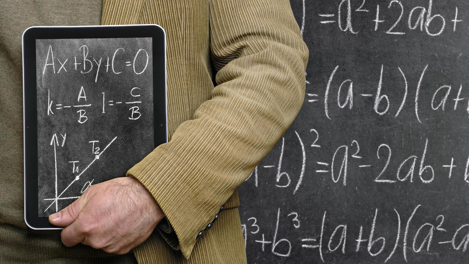 Lehrer hält einen Tablet-Computer vor einer Tafel, auf dem eine Tafel abgebildet ist.