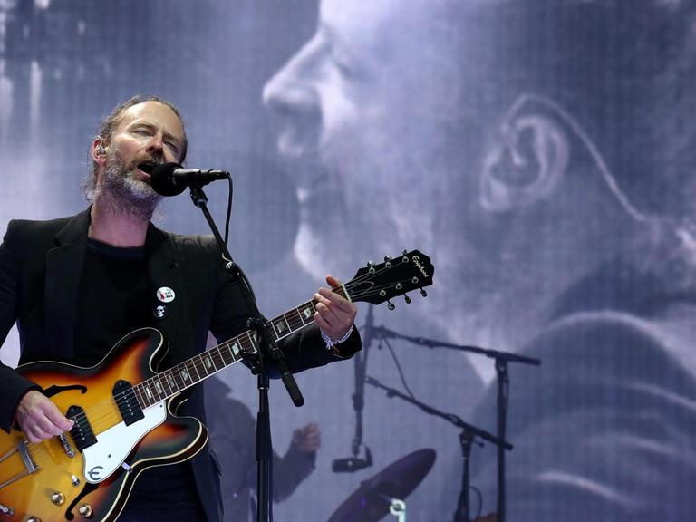 Ein bärtiger Mann steht mit einer halbakustischen Gitarren auf der Bühne und singt mit geschlossenen Augen in ein Mikrofon. Im Hintergrund ist sein Bild auf einer großen Leinwand zu sehen.