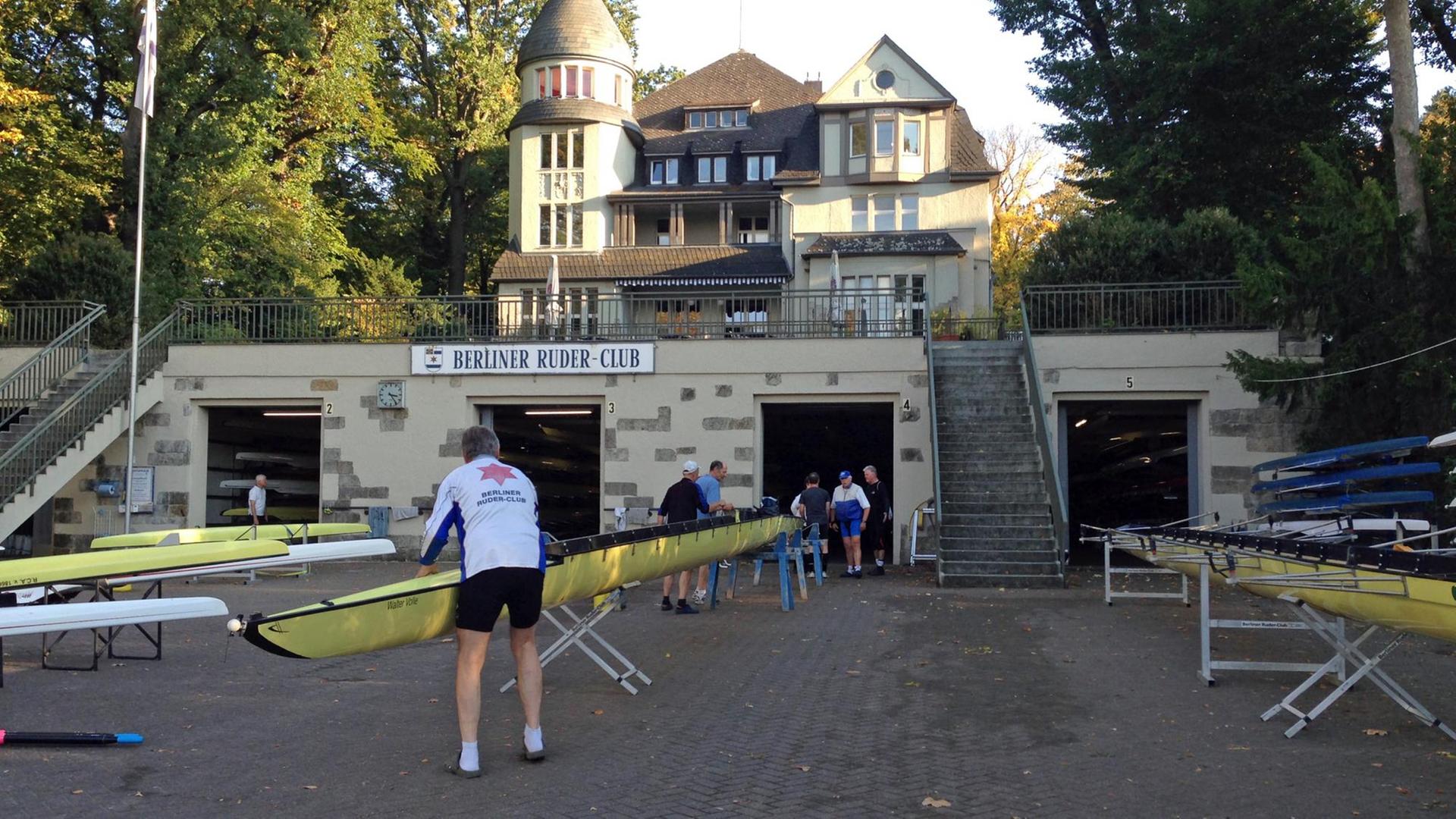 Blick auf das Gebäude des Ruder-Clubs, ein Ruderer zwischen Ruderbooten an Land