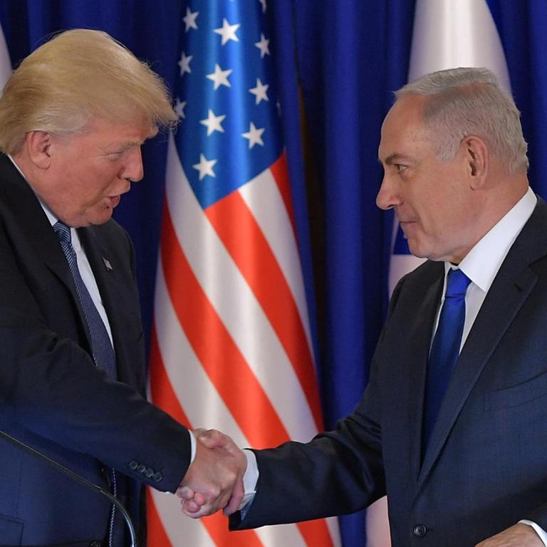 Trump und Netanjahu stehen vor den Flaggen ihrer Länder und reichen sich die Hand. 
