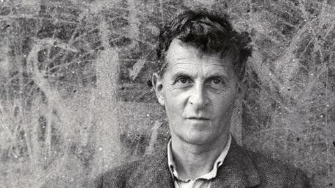 Schwarz-Weiß-Aufnahme von Ludwig Wittgenstein, vor einer zerkratzten Wand stehen.