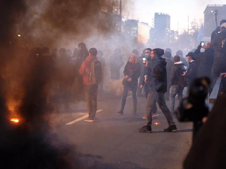 Bei einer Demonstration der Stuttgarter Initiative „Querdenken“ kommt es zu Auseinandersetzungen zwischen Teilnehmern und der Polizei. Auf der Straße stehen Demonstrierende im Rauch.