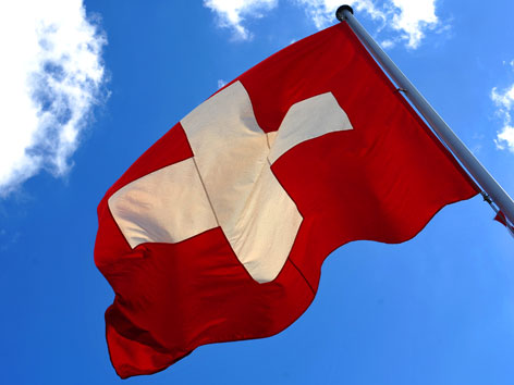 Die schweizer Flagge im Wind vor blauem Himmel.