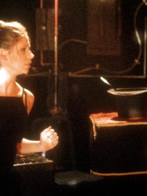 Die Schauspielerin Sarah Michelle Gellar, blond in einem schwarzen Top (links im Bild), steht kampfbereit einem Monster gegenüber, dargestellt von einem Mann in einem Ganzkörperanzug mit gefleckter Amphibienhaut.