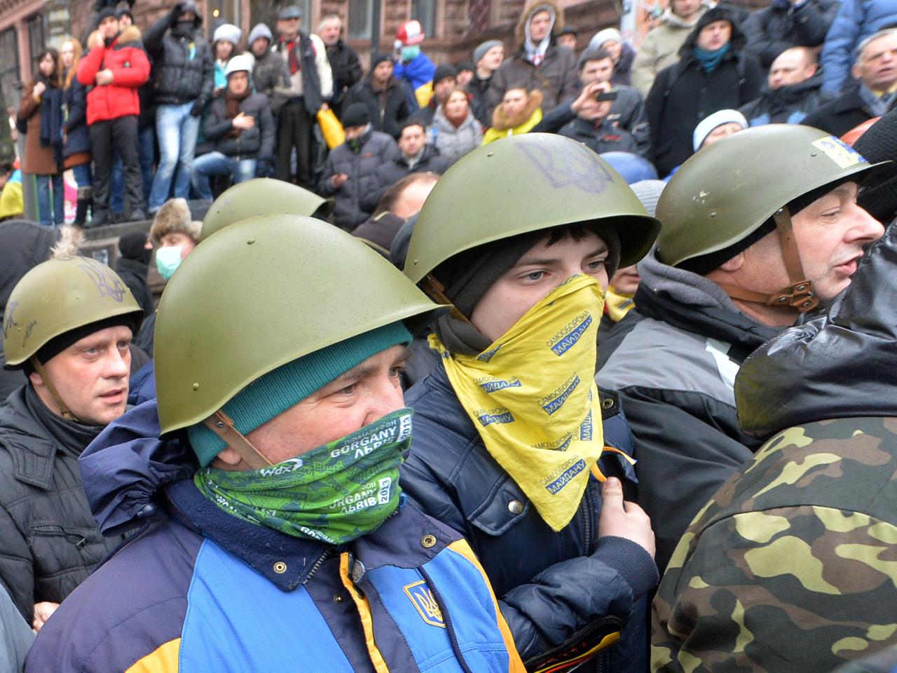 Demonstranten mit Mundschutz und Helmen auf dem Kopf.