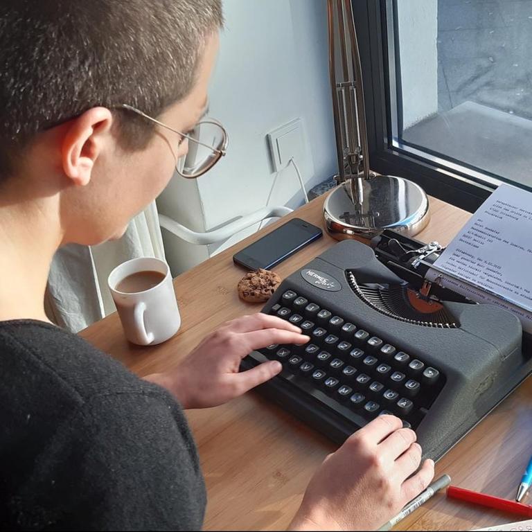 Eine junge Frau schreibt an einer alten Reiseschreibmaschine.