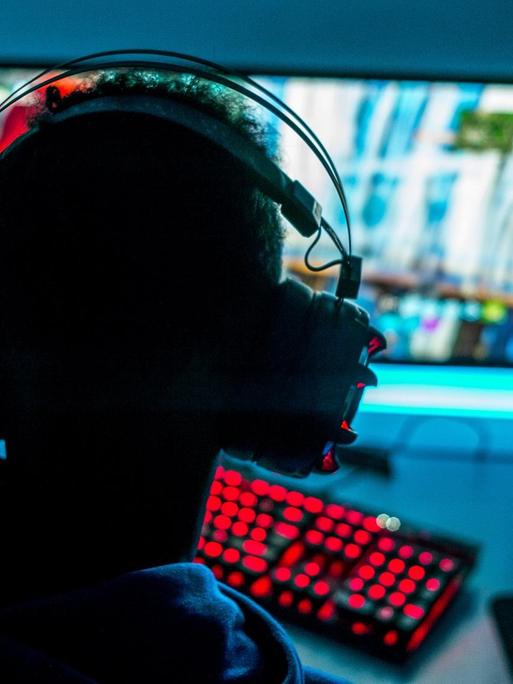 Ein Mann mit Kopfhörern sitzt vor einem Bildschirm und spielt am Computer