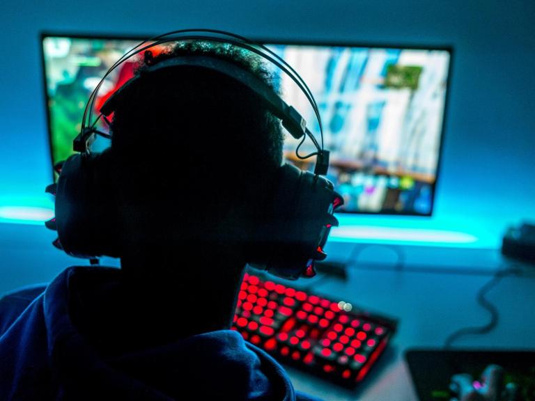 Ein Mann mit Kopfhörern sitzt vor einem Bildschirm und spielt am Computer