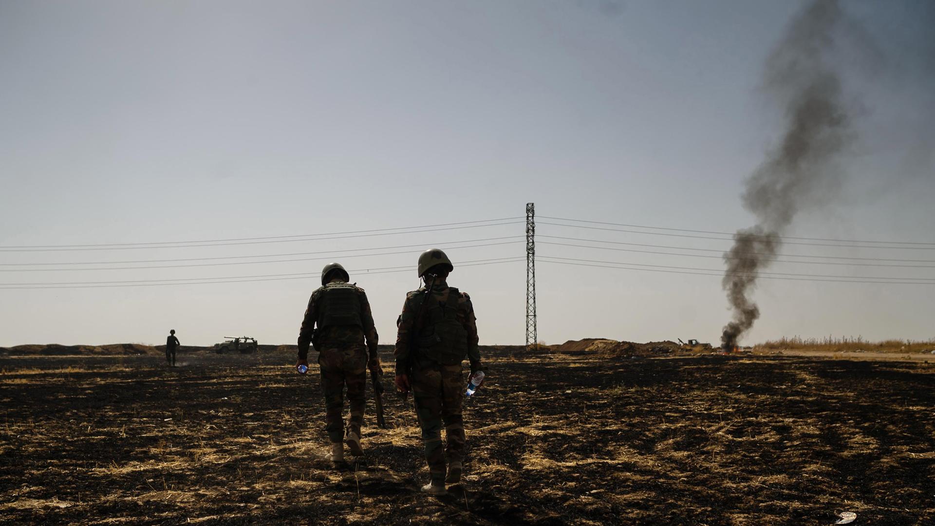 Eine karge Landschaft nahe Mossul. Zwei kurdische Soldaten laufen über ein Feld.