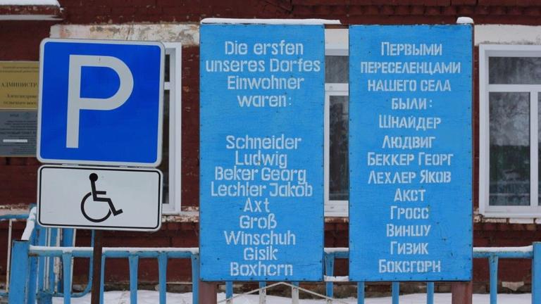 Ein Schild auf Deutsch und auf Russisch mit den Namen der ersten Einwohner steht im Dorf Aleksandrowka