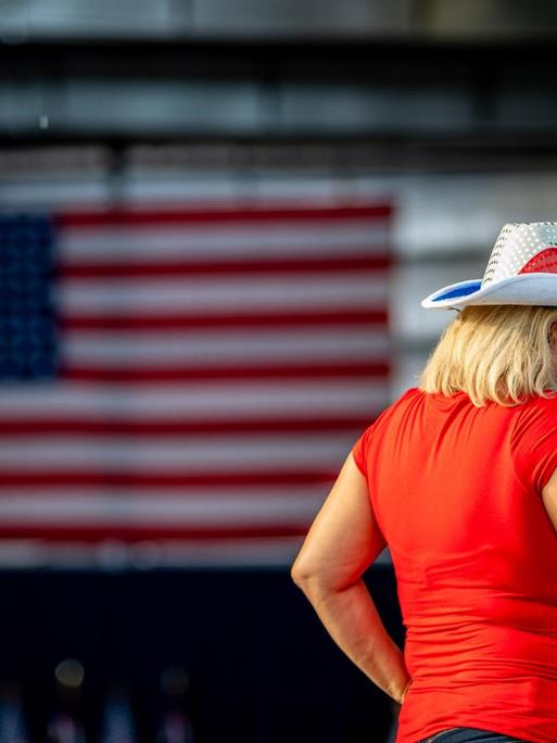 Eine Frau mit Cowboyhut schaut auf ihr Smartphone, im Hintergrund ist die amerikanische Flagge zu sehen.