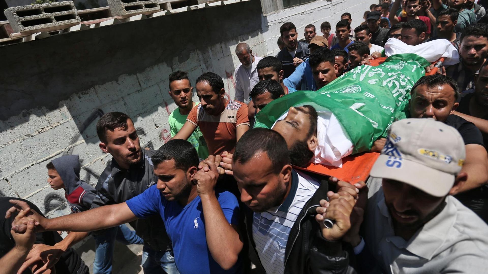 Mehrere Männer tragen den Sarg, auf dem eine Palästina-Fahre liegt. Darum viele  weitere Menschen im Trauerzug und am Straßenrand.