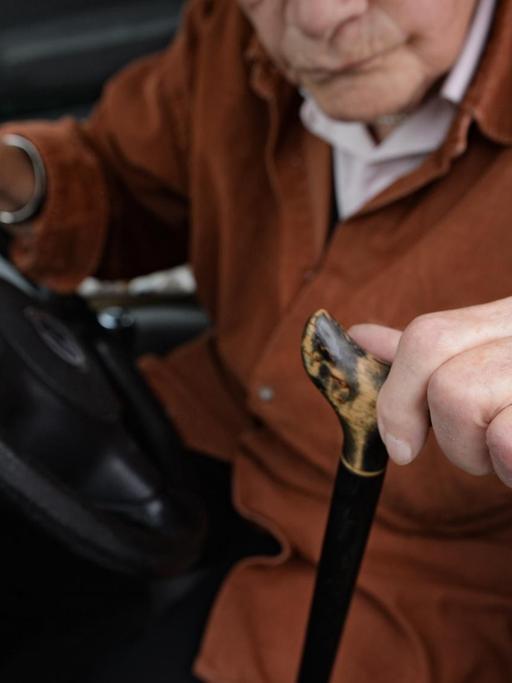 Eine 84-jährige Frau sitzt am Steuer ihres Kleinwagens. In der linken Hand hält sie ihren Gehstock, den sie zum Aussteigen benötigt.