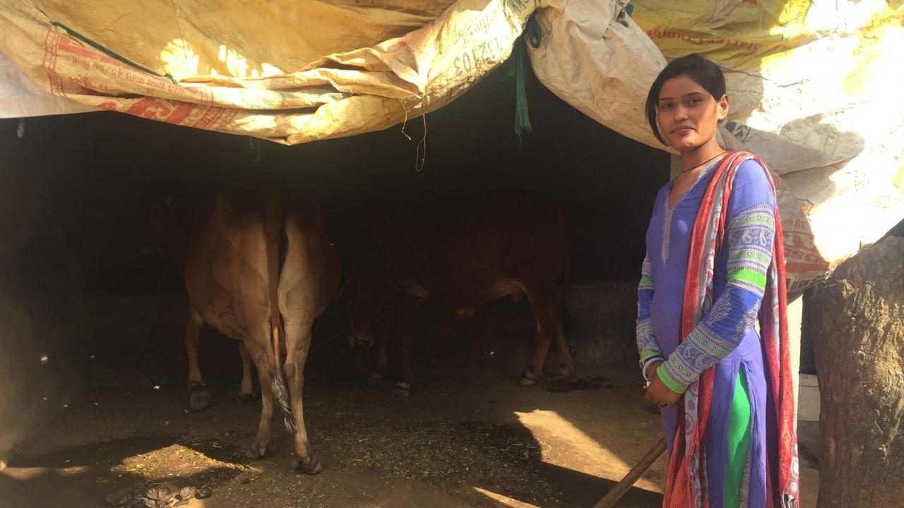 Rajni posiert für ein Foto, im Hintergrund sind Kühe zu sehen.