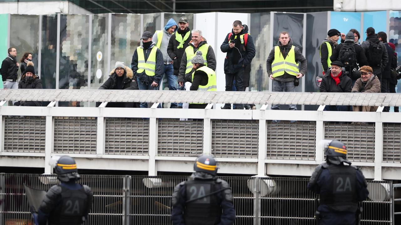 Das Foto zeigt Demonstranten in gelben Warnwesten vor dem Sitz von France Télévisions, dem öffentlich-rechtlichen Sender in Paris. Ihnen gegenüber stehen Polizisten der Sondereinheit CRS.