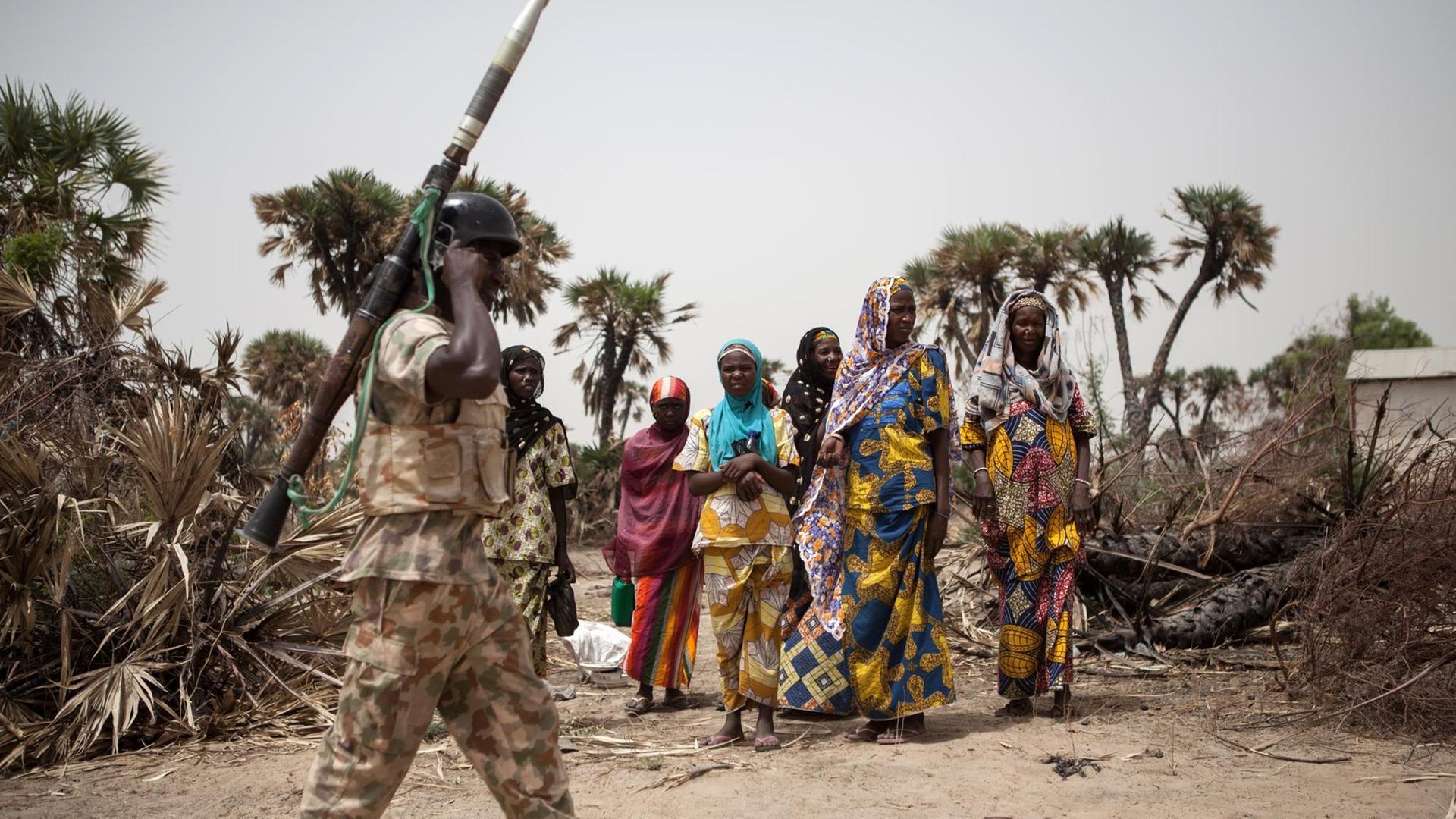 Soldat läuft mit einer reaktiven Panzerbüchse an der Schulter an einer Gruppe nigerianischer Frauen vorbei