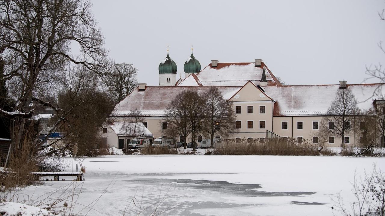 Das bayerische Kloster Seeon vor einem zugefrorenen, schneebedeckten See.