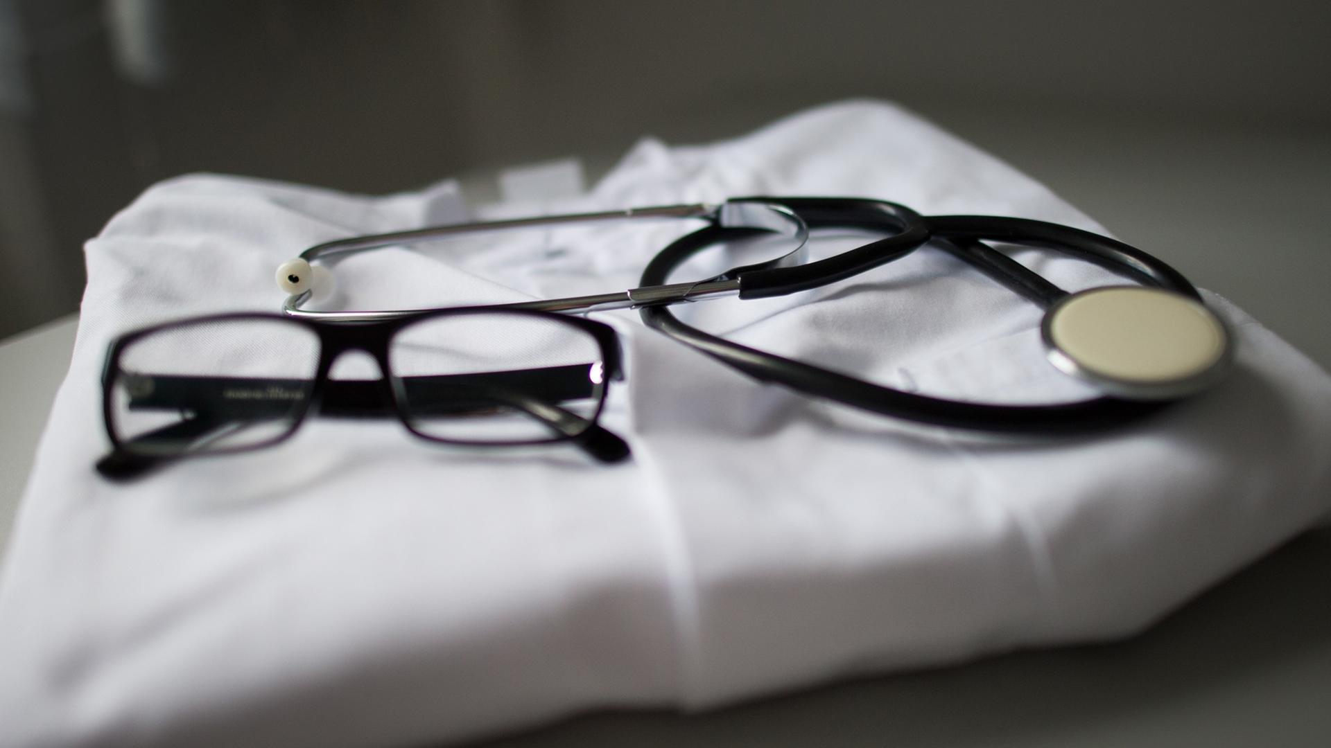 Ein Stethoskop und eine Brille liegen auf einem Arztkittel.