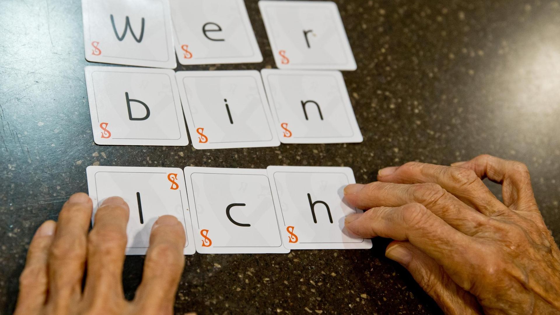 Zwei Hände legen die Karten eines Spiels zu dem Satz "wer bin ich" zusammen.
