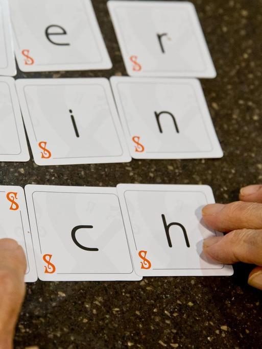 Zwei Hände legen die Karten eines Spiels zu dem Satz "wer bin ich" zusammen.