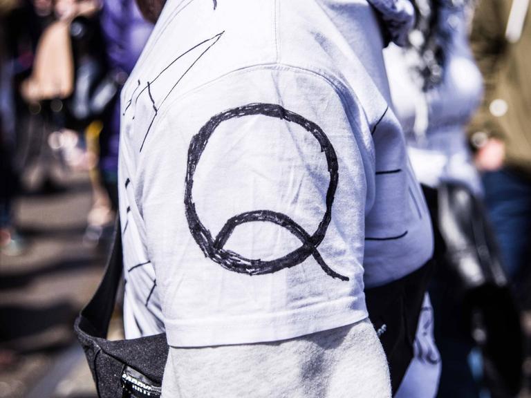 Eine Person trägt auf dem Ärmel ihres Shirts das Logo von QAnon.