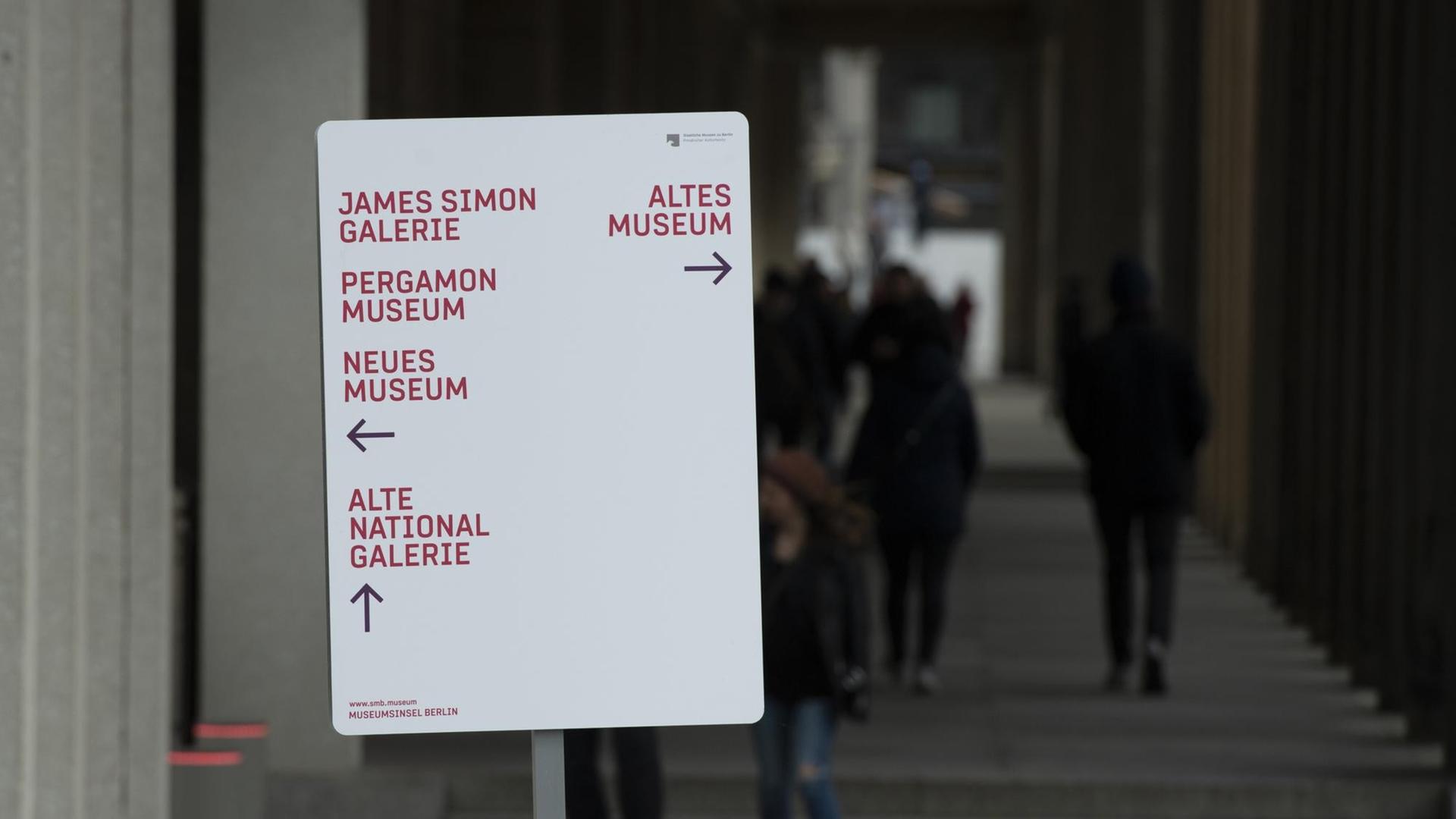 Das Schild mit den Namen einiger Museen und Pfeilen in verschiedene Richtungen steht in einem Säulengang.
