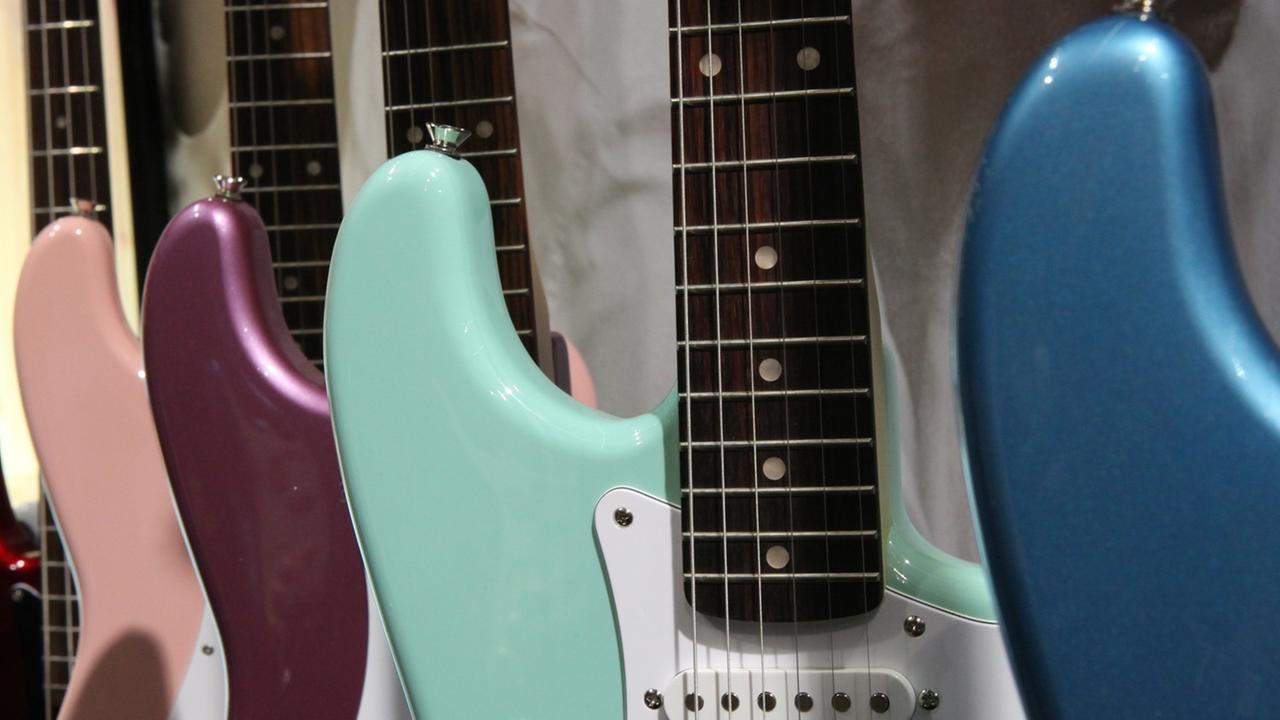 In einem Gitarrenständer stehen Elektrogitarren der Marke Fender Stratocaster in verschiedenen Pastelltönen