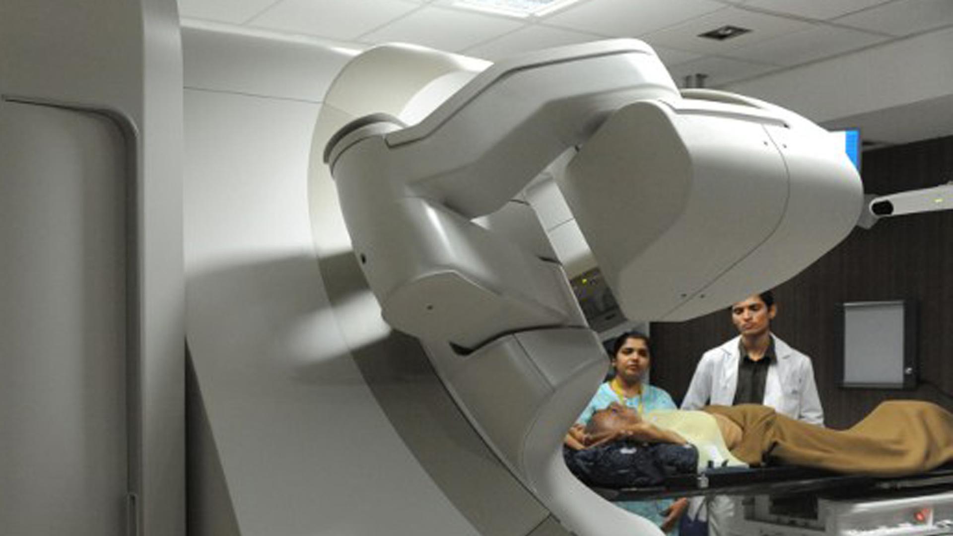 Zwei Ärzte und eine Patientin in einem Raum mit einem Bestrahlungsgerät.