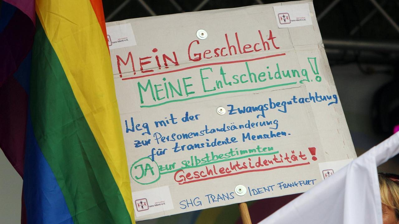 Beim Christopher Street Day 2018 in Frankfurt wird ein Plakat hochgehalten mit der Aufschrift "Mein Geschlecht.  Meine Entscheidung! Weg mit der Zwangsbegutachtung für transidente Personen" 