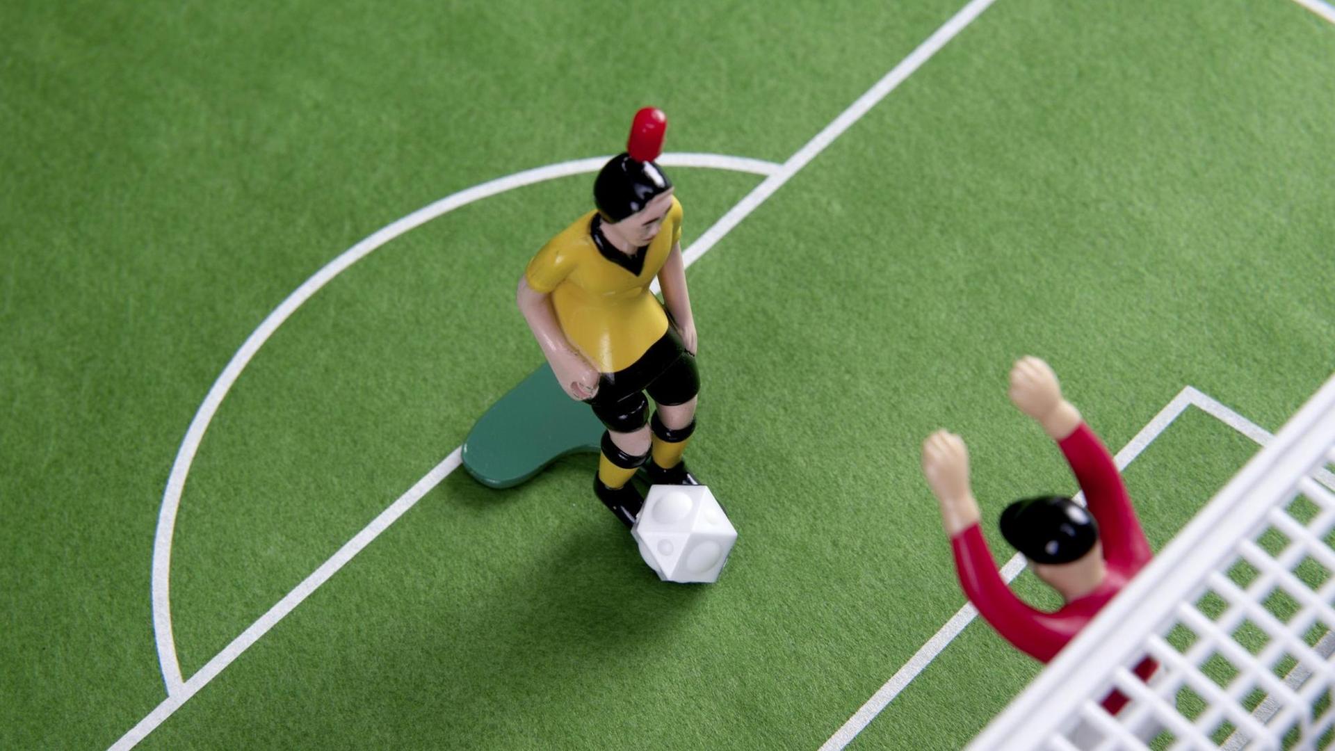 Stürmer und Torwart stehen sich auf dem Rasen eines Tipp Kick Spiels gegenüber.
