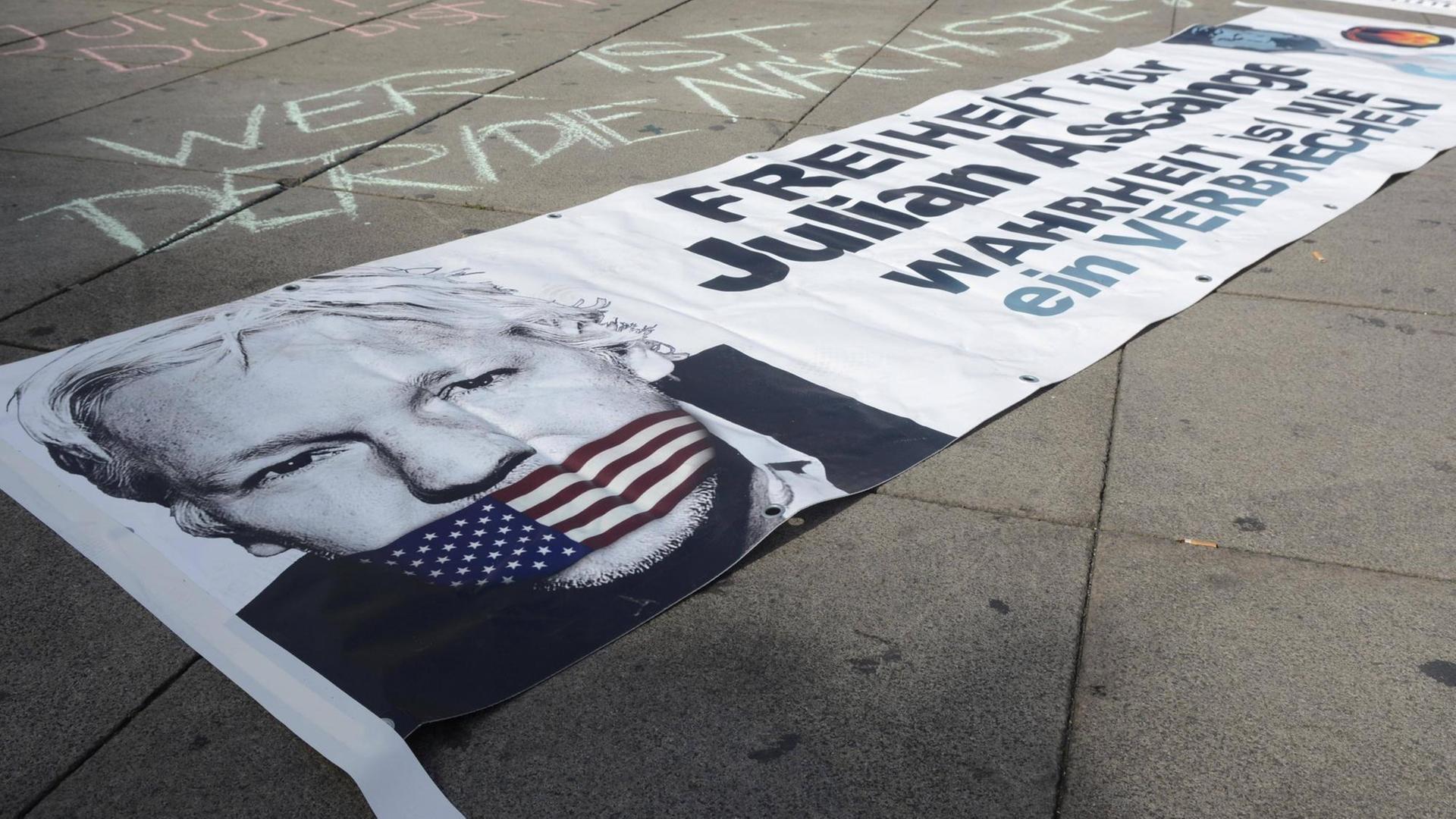 Auf einem Plakat, das auf der Straße liegt, ist das Bild von Julian Assange zu sehen mit einem Maulkorb in den US-Farben.