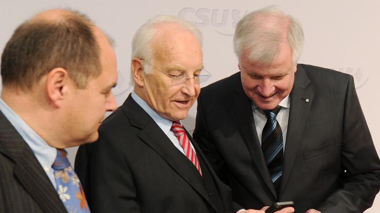 Der parlamentarische Verdeidigungsstaatssekretär, Christian Schmidt, der CSU-Ehrenvorsitzende Edmund Stoiber und der CSU-Parteivorsitzende Horst Seehofer betrachten ein Handy.