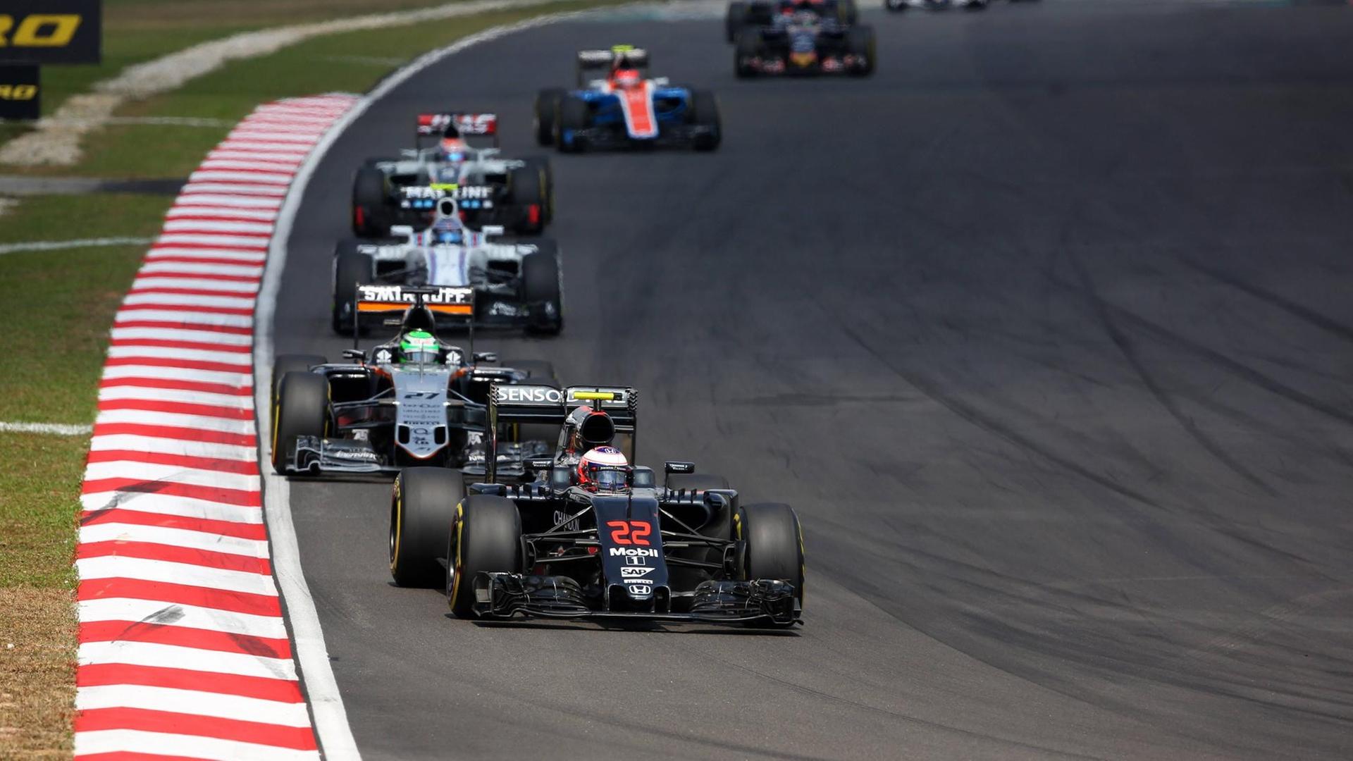 Zu sehen sind mehrere Formel-1-Autos, die hintereinander auf einer Rennstrecke rasen. Zu sehen sind mehrere Formel-1-Autos, die hintereinander auf einer Rennstrecke rasen.