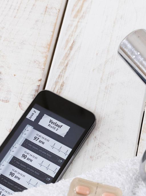 Smartphone mit einer Fitness-App, daneben eine Hantel auf einem Handtuch