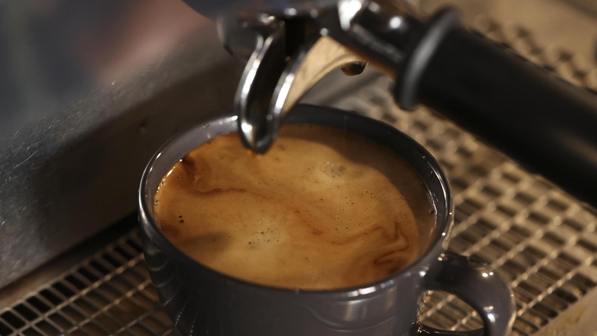 In einem Café fließt Kaffee aus einer professionellen Maschine in eine schwarze Tasse.