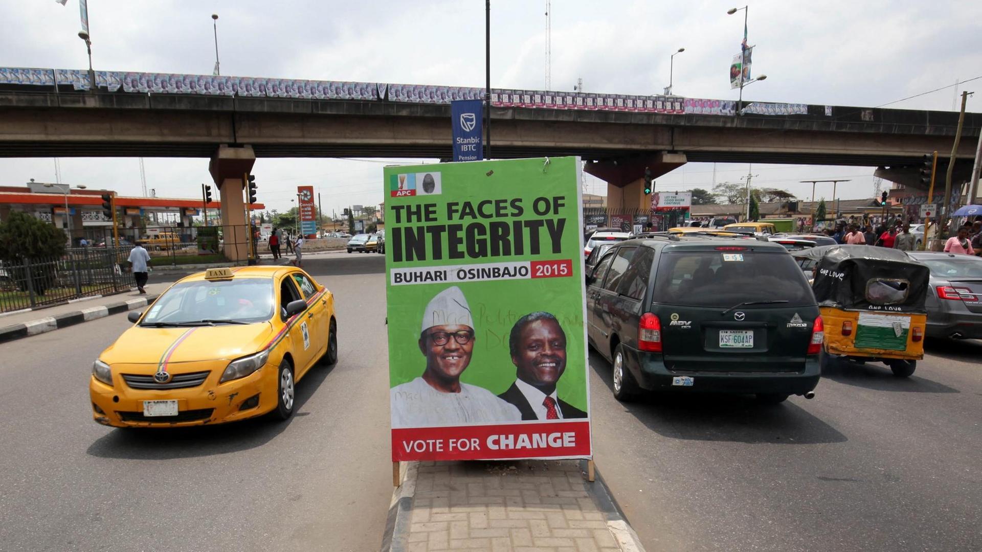 Autos fahren am 14.02.2015 an einem Wahlplakat in Lagos, Nigeria vorbei. Das Plakat zeigt den Präsitentschaftskandidaten Muhammadu Buhari (L) und Vize-Kandidat Yemi Osinbajo (R).