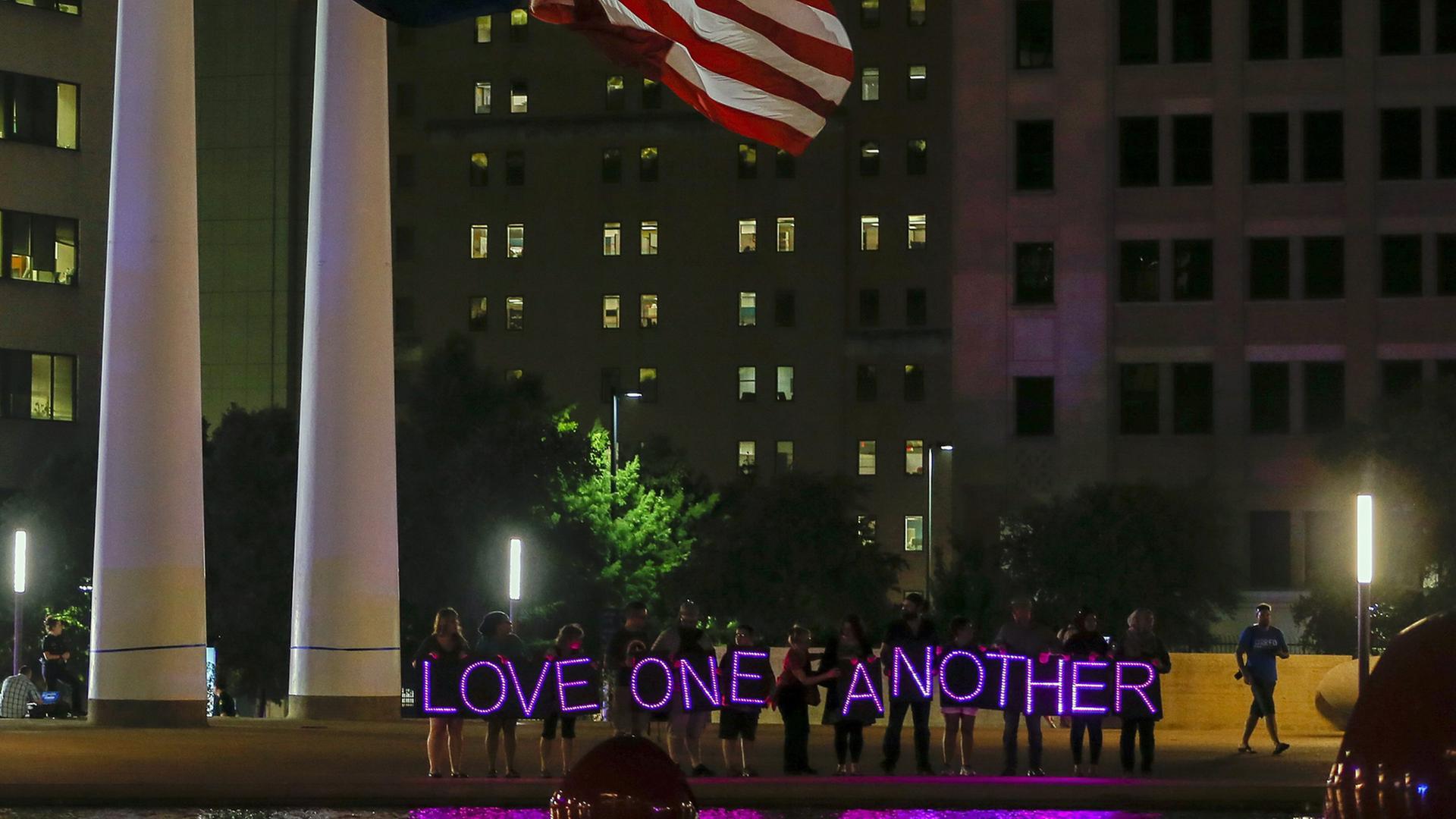 Menschen halten bei einer Nachtwache auf dem Platz vor der City Hall in Dallas LED-Lichter mit dem Schriftzug "Love one another" - liebt einander - hoch, aufgenommen am 11. Juli 2016.
