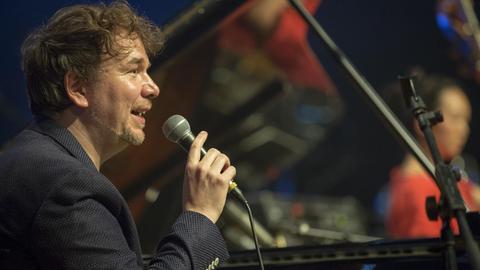 Der Pianist Florian Weber sitzt am Flügel und hält ein Mikrofon in der Hand