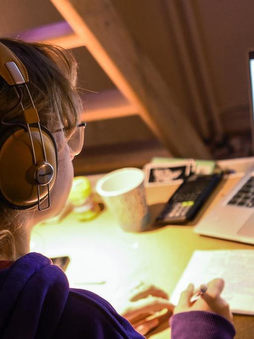 Ein Mädchen sitzt zu Hause an ihrem Schreibtisch und macht an ihrem Laptop Aufgaben für die Schule.