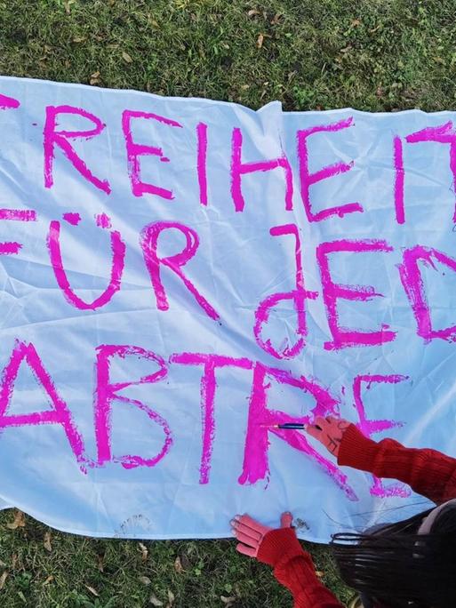 Eine junge Frau bemalt ein Transparent auf dem "Freiheit für jede Antreibung" in pinker Farbe zu lesen ist.