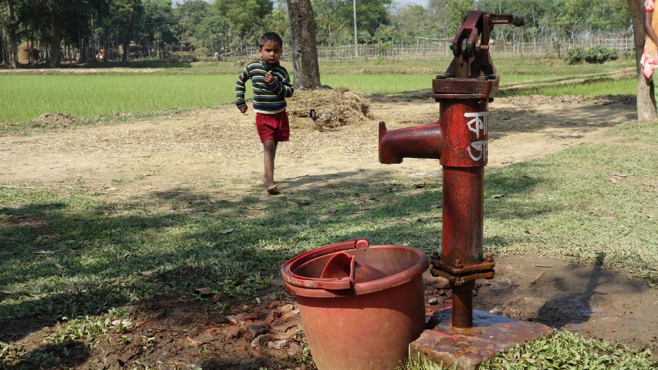 Millionen mit Arsen kontaminierte Brunnen wurden in Bangladesch mit roter Farbe gekennzeichnet, werden aber trotzdem benutzt. Ein Kind läuft gerade zur Pumpe.