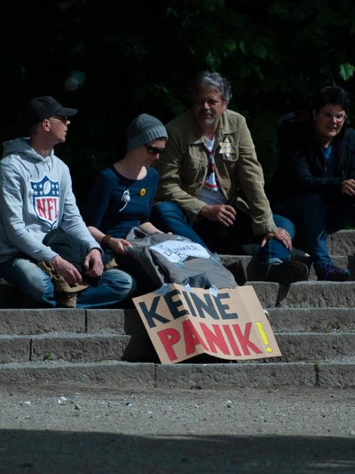Bei einer Demonstration gegen Corona-Maßnahmen: Vier Demonstranten sitzen auf Steinstufen, vor sich ein Transparent mit der Aufschrift "Keine Panik". Win Demonstrant hat einen gelben Stern auf der Jacke. Auf diesem steht "Ungeimpft".