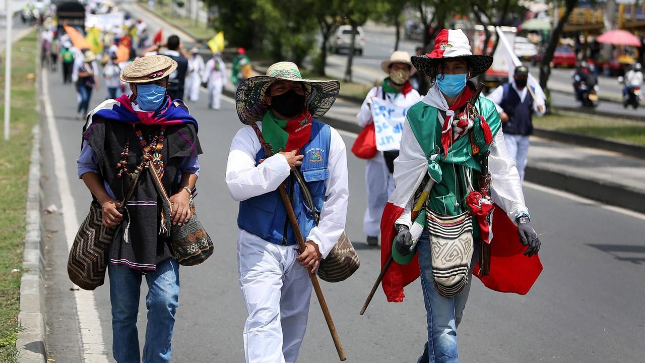 Demonstranten in traditioneller bunter Kleidung der Indigenen laufen auf einer Straße in Cali.